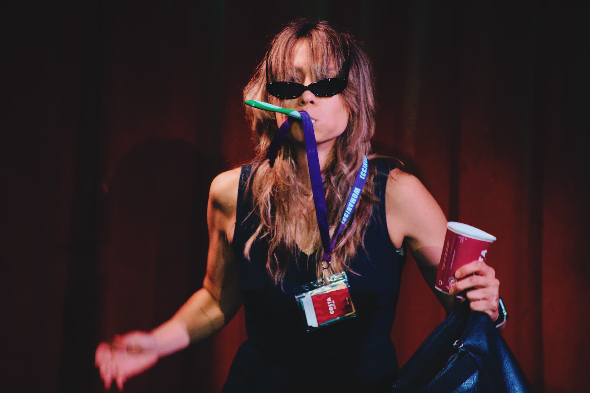 Lilla Multipass on stage with a toothbrush in her mouth, sunglasses, and a lanyard